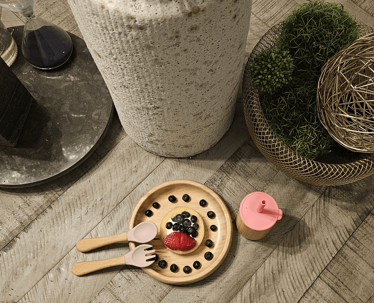 Wooden plate with berries, a pink lid, and utensils on a wooden surface.